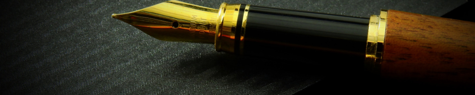 Füllfederhalter mit goldener Spitze auf einem schwarzen, strukturierten Hintergrund.