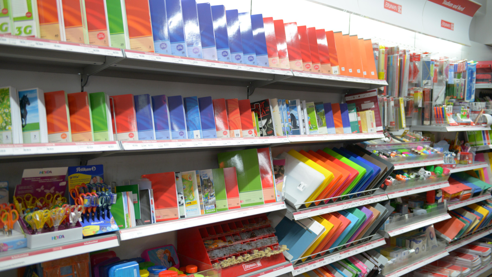 Regal mit bunten Ordnern, Papier, Stiften und Bastelmaterial in einem Geschäft.