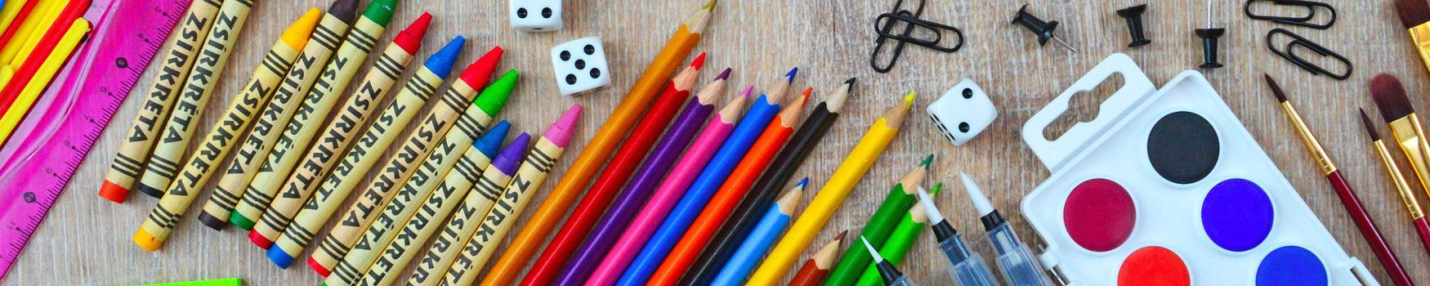 Bunte Schulmaterialien auf einem Tisch mit Buntstiften, Wasserfarben, Notizzetteln und Büroklammern.
