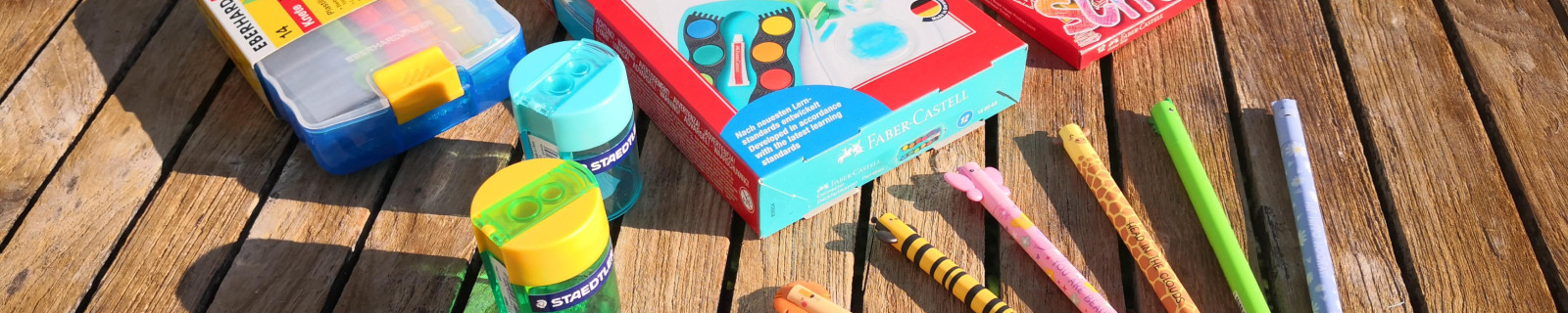Künstlerbedarf mit Stiften und Farben auf einem Holztisch im Freien.