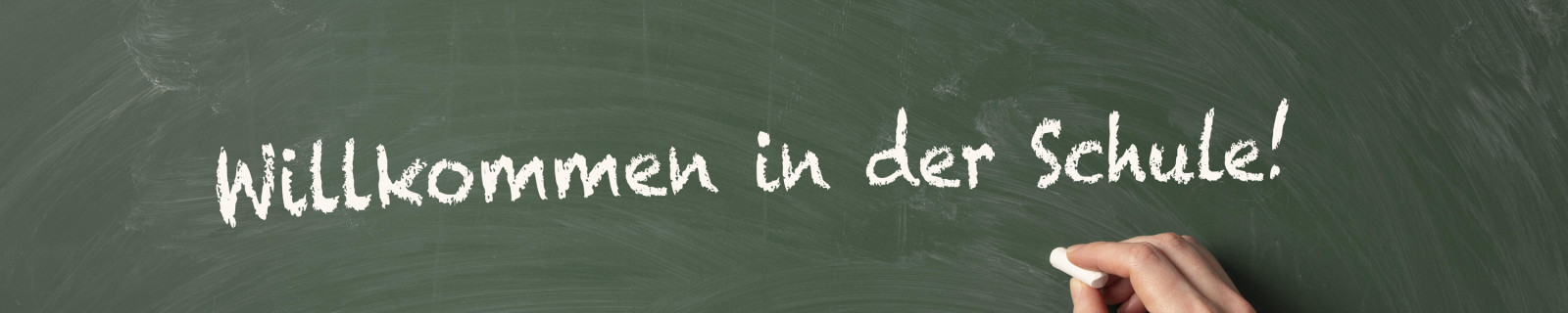 Eine Hand schreibt 'Willkommen in der Schule!' auf eine Tafel.