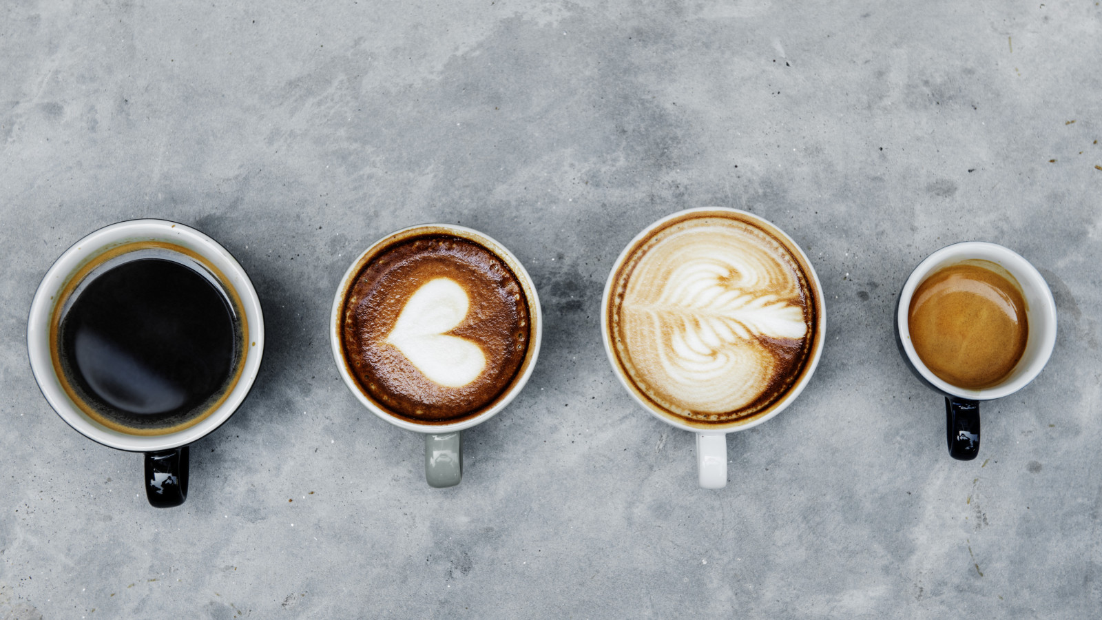 Vier Kaffeetassen nebeneinander mit schwarzem Kaffee, zwei Sorten mit Latte Art und Espresso.