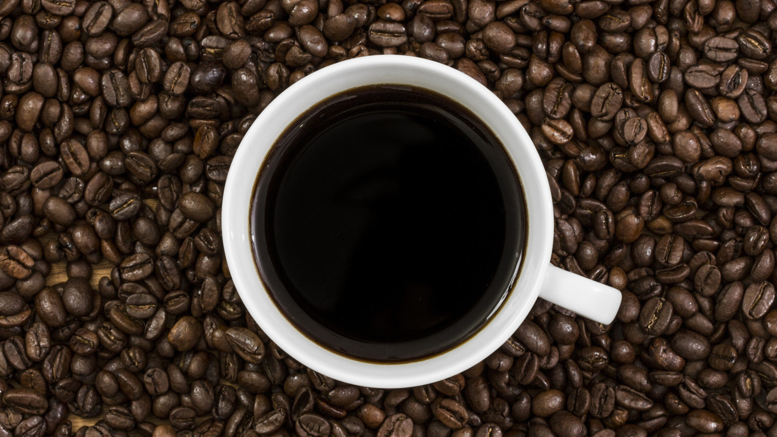Weiße Tasse Kaffee auf Kaffeebohnenhintergrund.