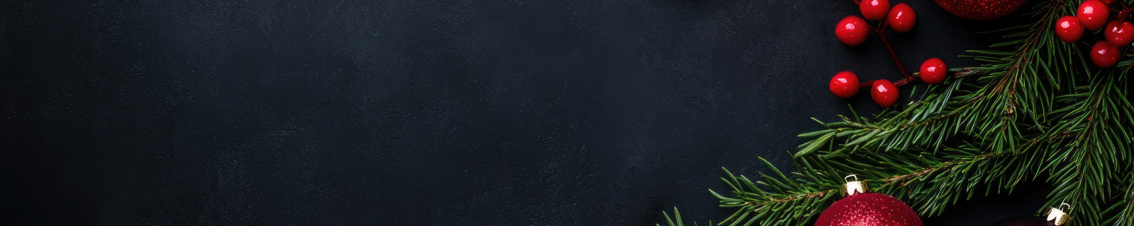 Tannenzweige mit roten Kugeln und Beeren auf dunklem Hintergrund.