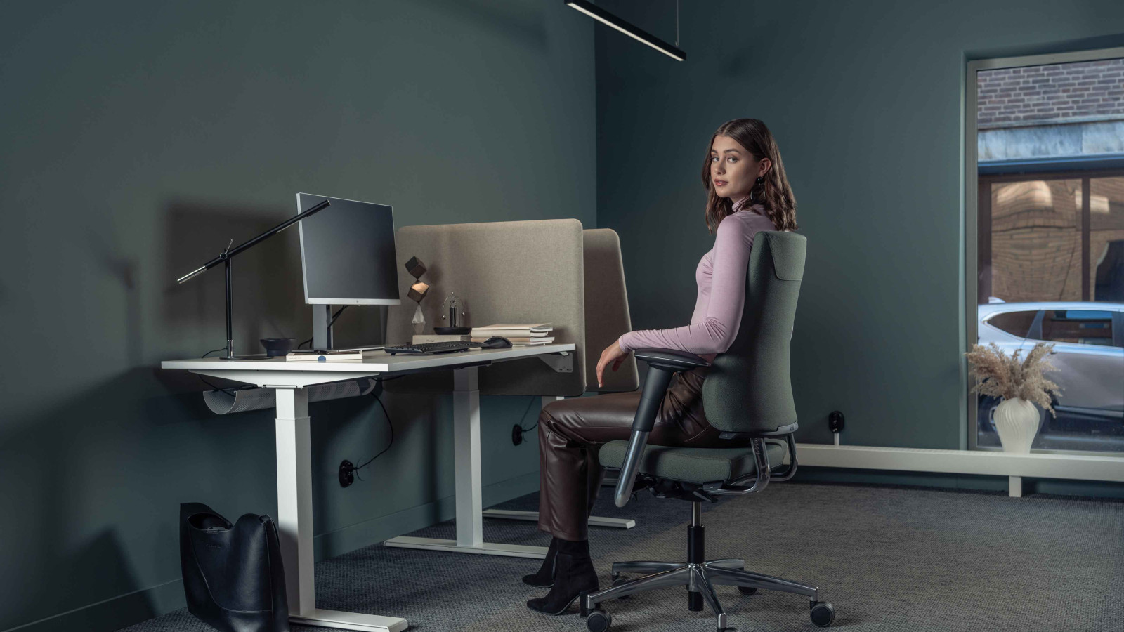 Frau in einem modernen Büro, sitzend auf einem ergonomischen Stuhl an einem Tisch mit Monitor.