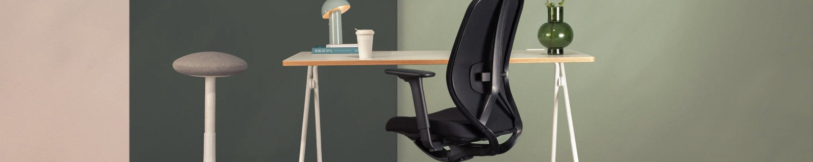 Büroszene mit ergonomischem Stuhl, Tisch, Lampe und Vase auf Teppichboden.