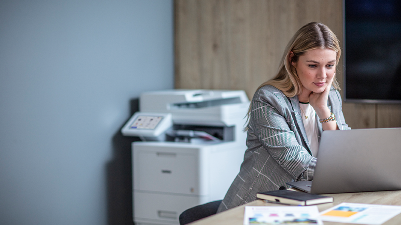 Frau im Büro am Laptop mit Drucker im Hintergrund