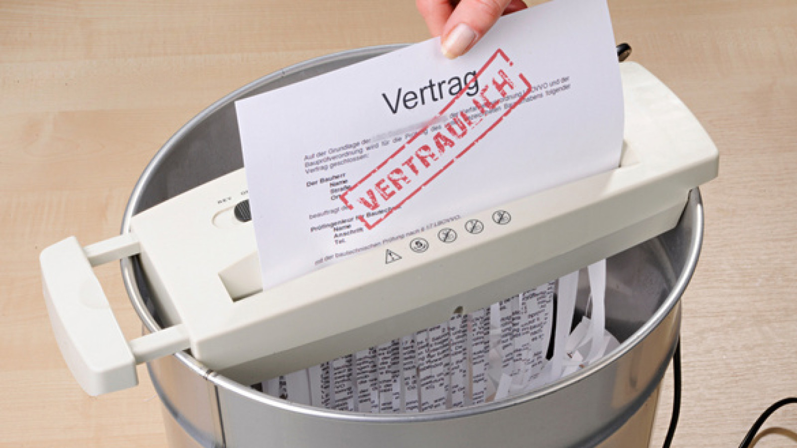 Eine Hand legt ein Papier mit der Aufschrift 'Vertrag' in einen Aktenvernichter.