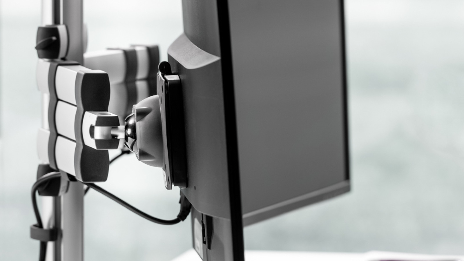 Seitenansicht eines Arbeitsplatzes mit Monitor an einem verstellbaren Arm, Tastatur und Maus auf dem Tisch.