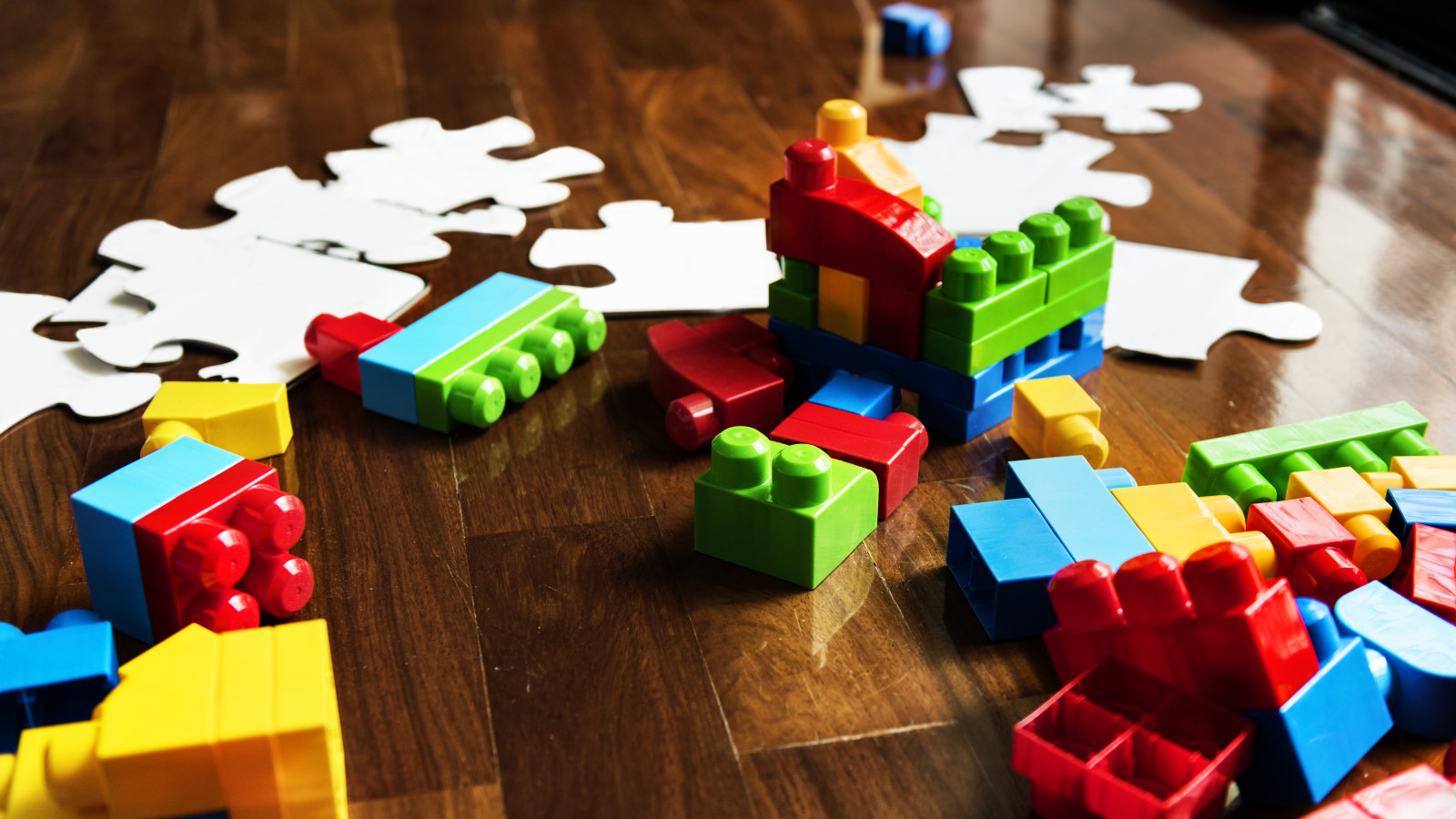 Bunte Bauklötze und weiße Puzzleteile liegen verstreut auf einem Holzboden.