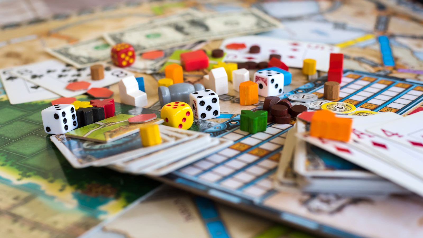 Nahaufnahme eines Brettspiel-Tisches mit Würfeln, Karten und bunten Spielsteinen.