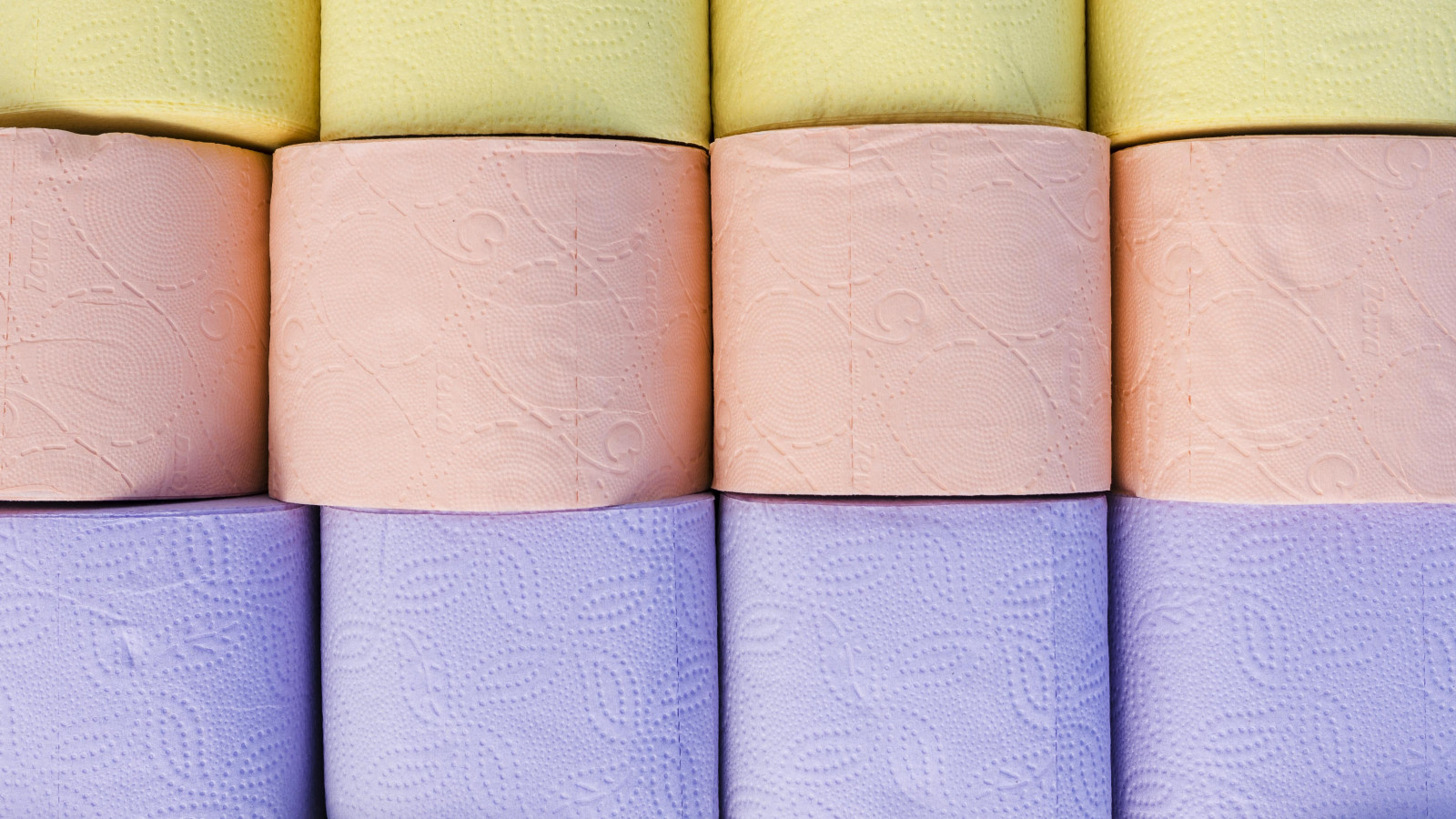 Gestapelte Toilettenpapierrollen in Gelb, Rosa und Lila.